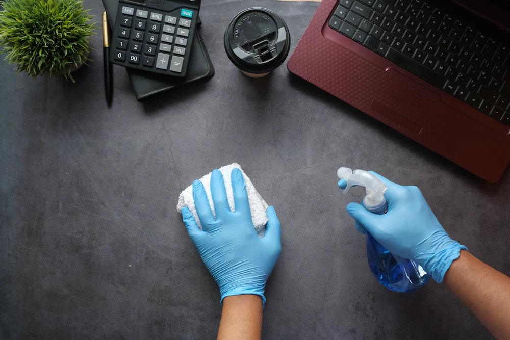 Cleaner in gloves disinfecting a desk